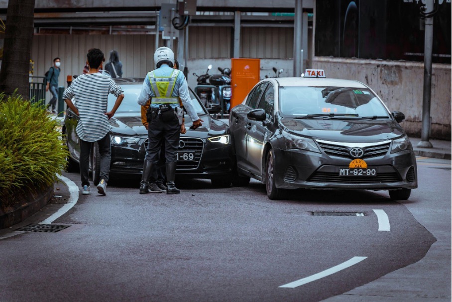 Řidič a policista stojí vedle zaparkovaných vozidel po drobné dopravní nehodě na městské ulici.